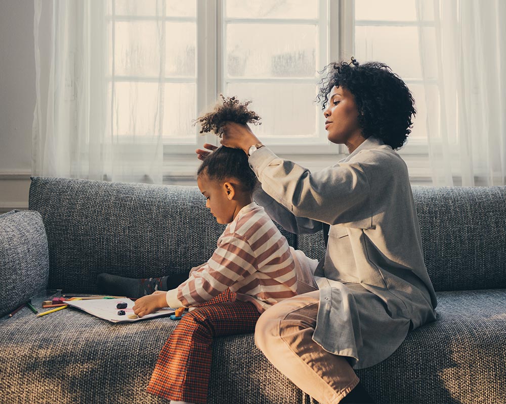 Mother styling her child's hair while the child colors, capturing a serene domestic scene and parental care.
