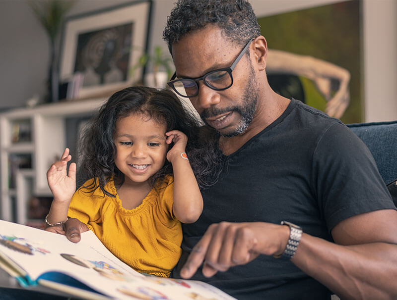 Smiling father reading a book with his young daughter, highlighting a tender family moment and the joy of shared learning at home.