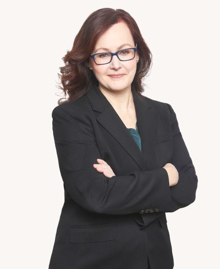 Portrait of lawyer Adrienne Lee in a black suit with arms crossed, wearing glasses, and presenting a professional and approachable demeanor on a light orange background.